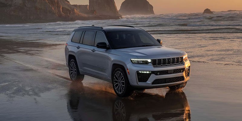 Jeep SUV driving along a beach with ocean waves and rocky cliffs in the background